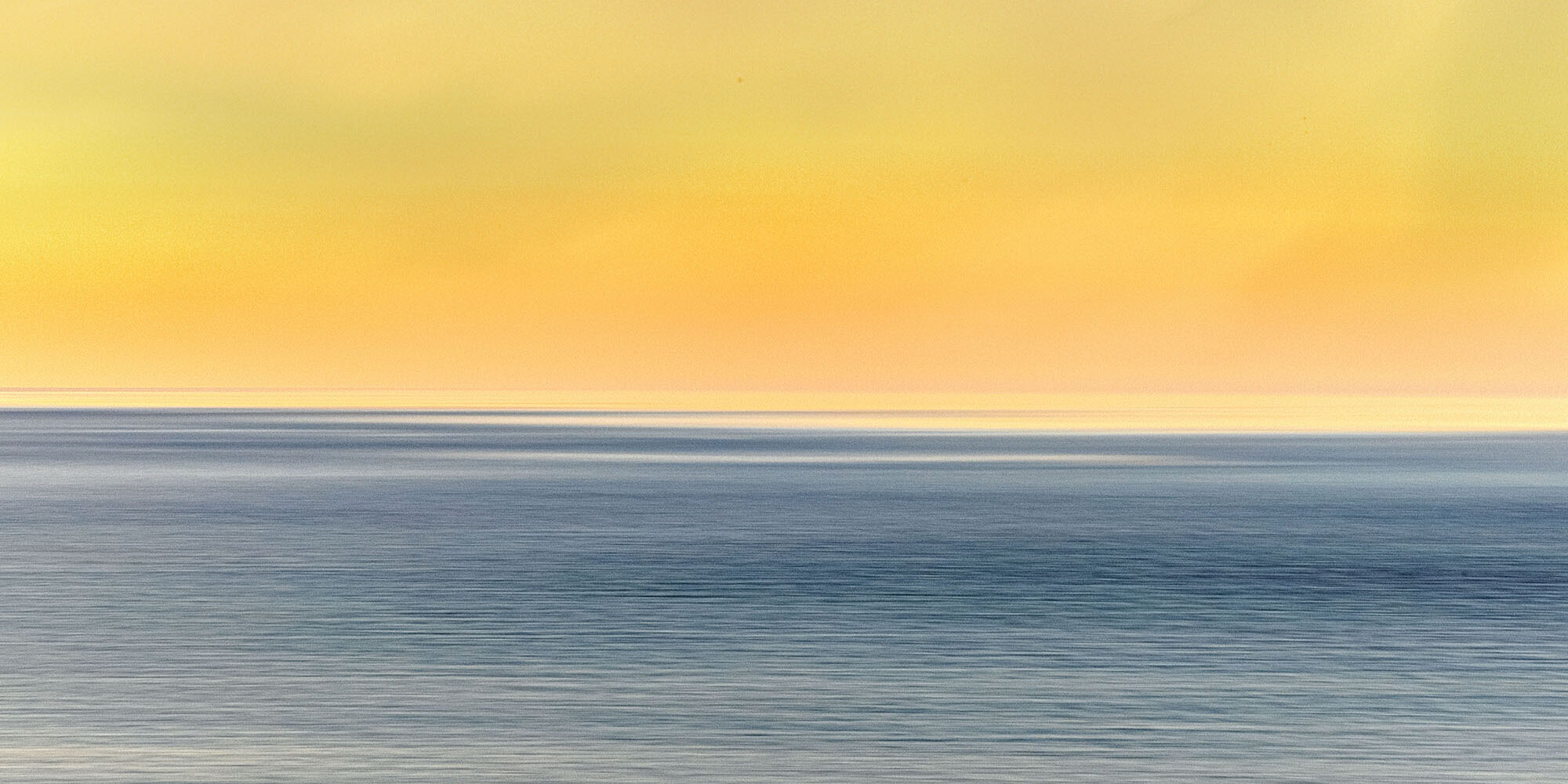 Fotografía minimalista del mar al atardecer con tonos cálidos en el cielo y una gaviota en vuelo, capturando la serenidad y belleza de la costa.