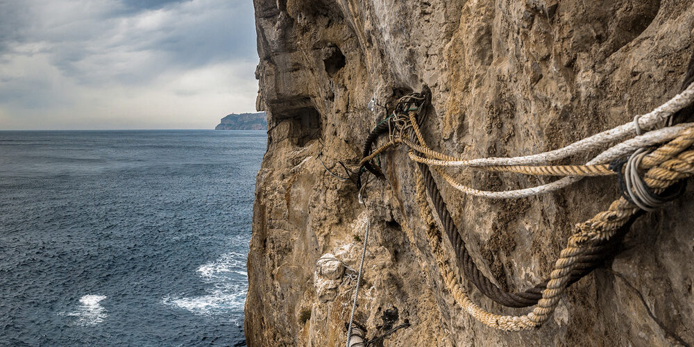 Vista de cuerdas y maderas usadas como soporte en un acantilado frente al mar, resaltando las técnicas tradicionales de los pescadores.