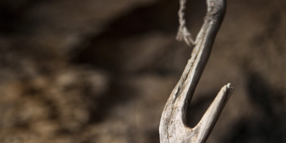 Gancho de madera suspendido en una cuerda, detalle de las herramientas tradicionales de pesca en una cueva costera.