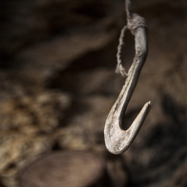 Gancho de madera suspendido en una cuerda, detalle de las herramientas tradicionales de pesca en una cueva costera.