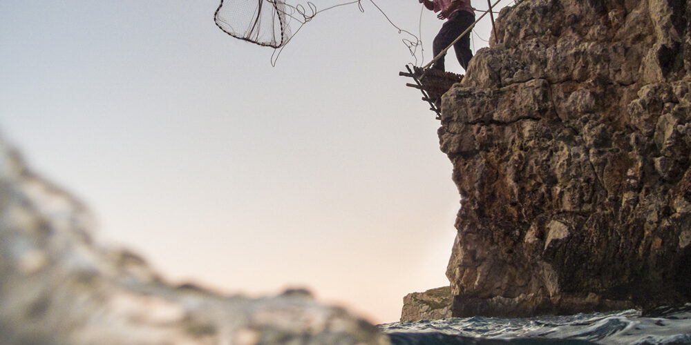 Pescador lanzando una red desde un acantilado, capturando la esencia de las técnicas de pesca artesanal.