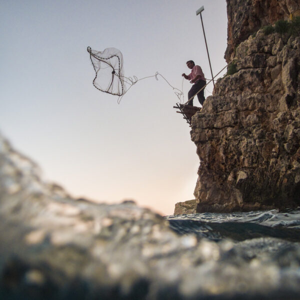 Pescador lanzando una red desde un acantilado, capturando la esencia de las técnicas de pesca artesanal.