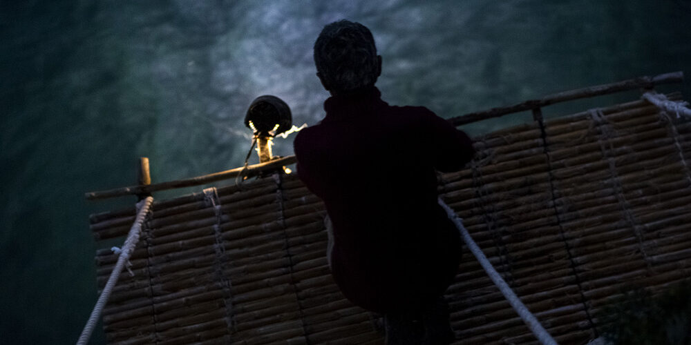 Persona en una plataforma de bambú iluminado por un foco en la noche.