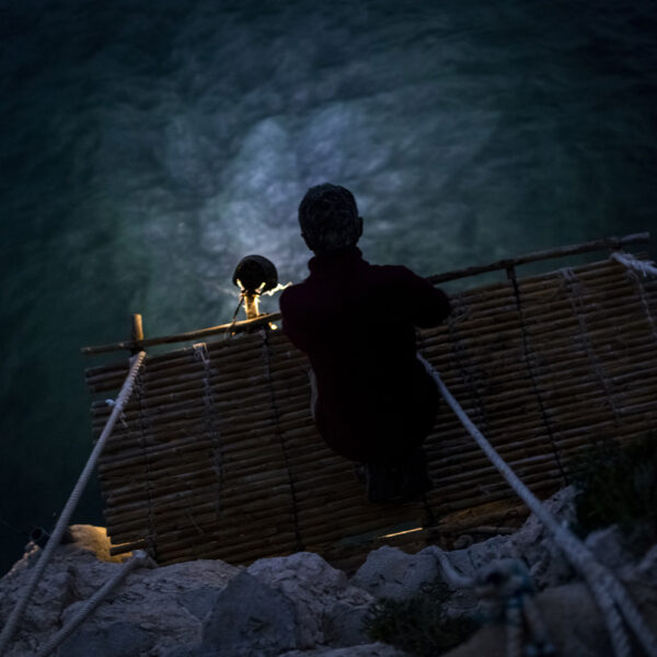 Persona en una plataforma de bambú iluminado por un foco en la noche.