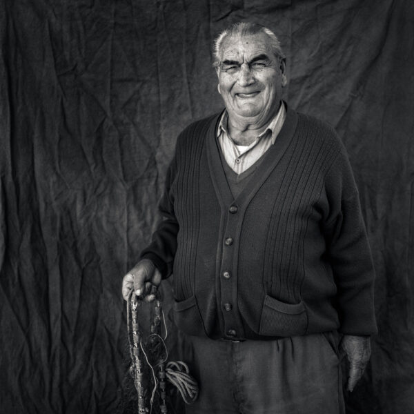 Retrato en blanco y negro de un hombre mayor sosteniendo herramientas de pesca.