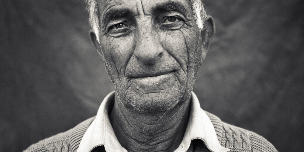 Primer plano en blanco y negro de un hombre mayor con suéter tejido, mostrando una expresión amable y reflexiva. Ideal para proyectos fotográficos rurales o históricos.