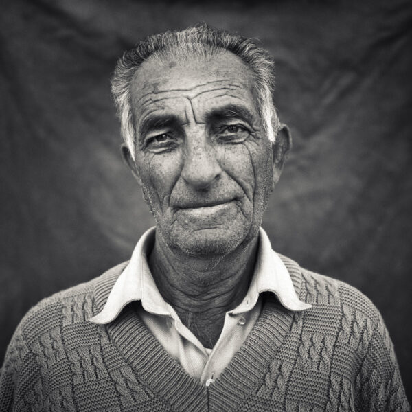 Primer plano en blanco y negro de un hombre mayor con suéter tejido, mostrando una expresión amable y reflexiva. Ideal para proyectos fotográficos rurales o históricos.