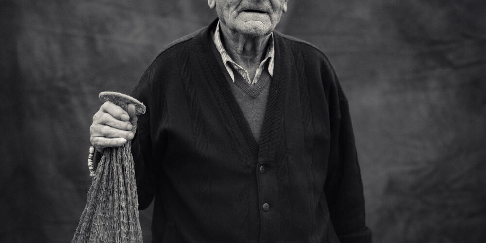 Fotografía artística de un anciano sosteniendo una red de pesca, en tonos monocromáticos.
