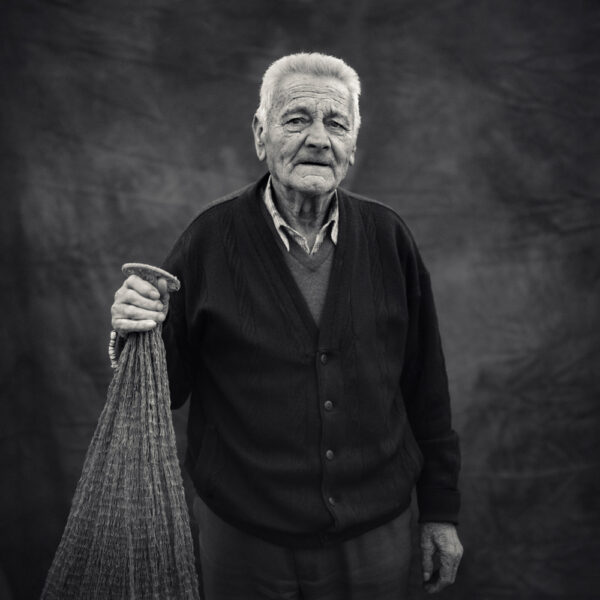 Fotografía artística de un anciano sosteniendo una red de pesca, en tonos monocromáticos.