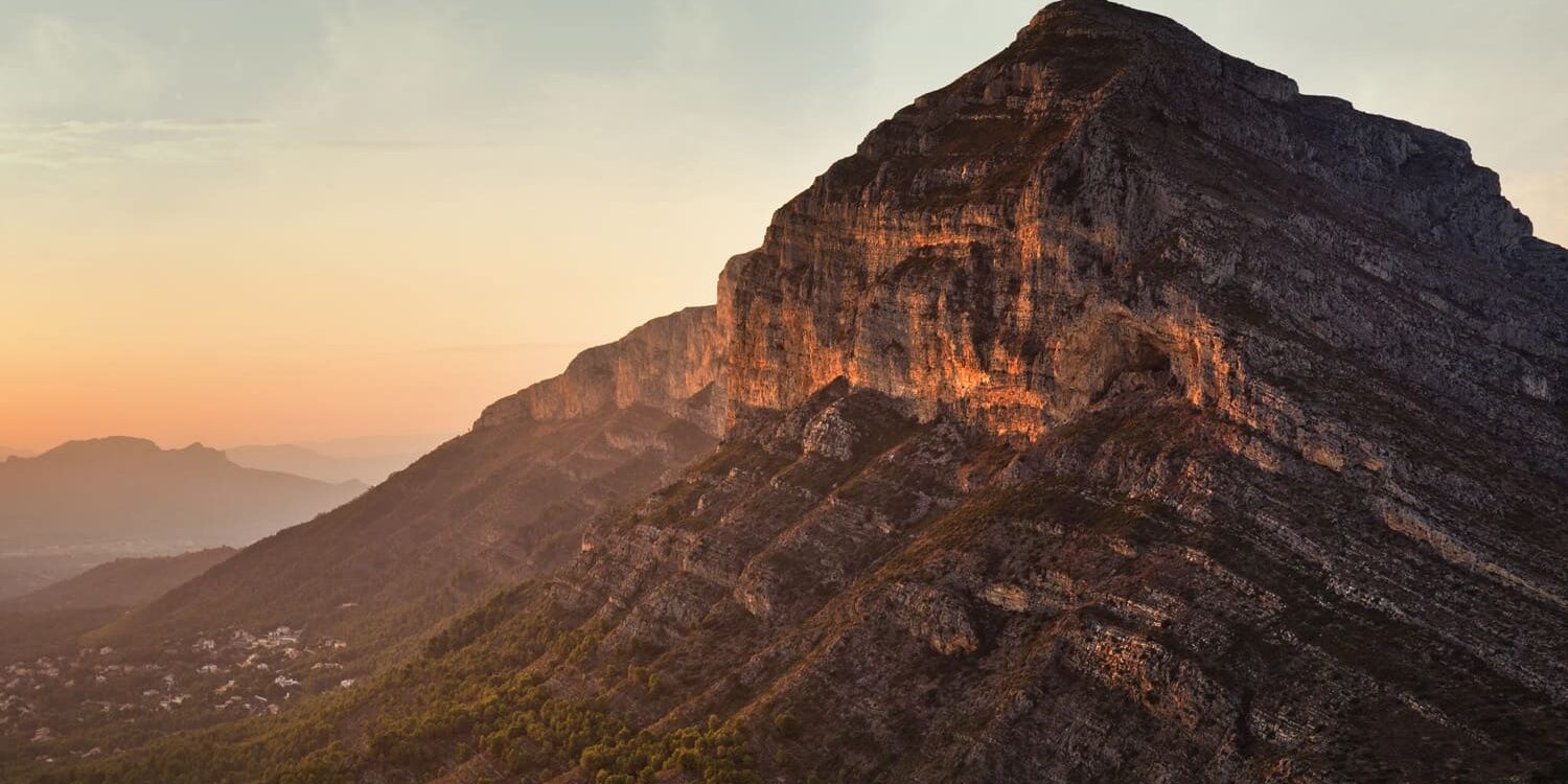 Fotografía del Montgó al atardecer, con la luz cálida iluminando sus escarpadas laderas y un cielo despejado que enmarca el paisaje. Una escena que captura la majestuosidad y serenidad de este icónico monte.