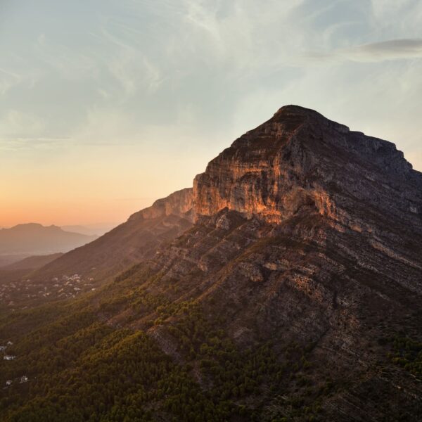 Fotografía del Montgó al atardecer, con la luz cálida iluminando sus escarpadas laderas y un cielo despejado que enmarca el paisaje. Una escena que captura la majestuosidad y serenidad de este icónico monte.